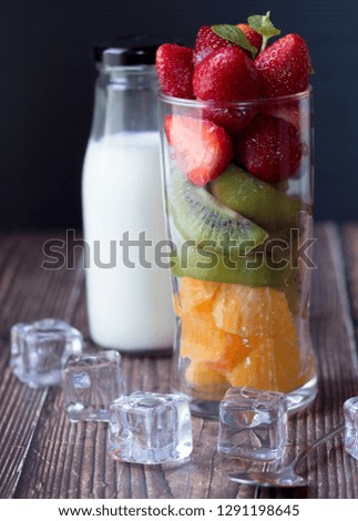 Mix fruits in glass for smoothie or cocktail drink, milk, strawberry, orange, kiwi, ice on wood table. Food photography for magazine, book advertising business. Selective focus.