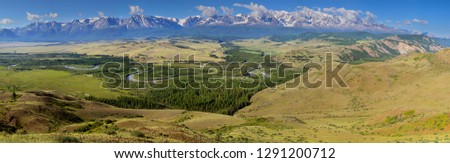 Over the mountain valley, snow-capped peaks in the clouds and green summer slopes, large panorama