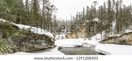 Panoramic picture of frozen and ice covered river in small canyon with waterfall