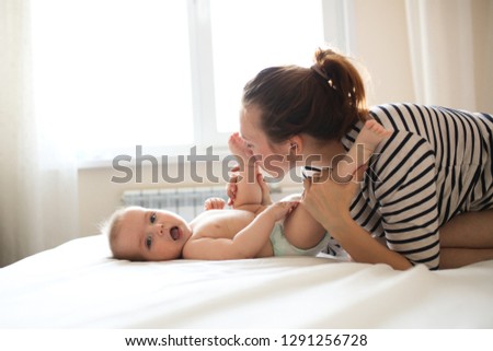 funny baby 6 months old with mom on a bed in a real room. Mom tickles and gently kisses the baby. Concept maternal love and motherhood, soft focus, toning and lifestyle