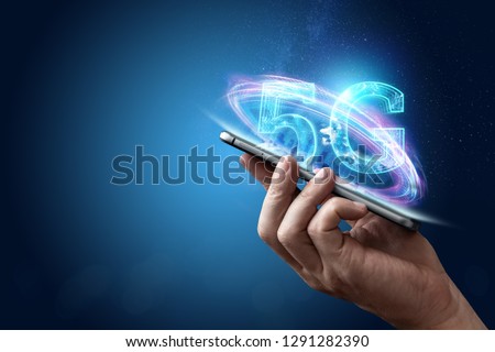 Creative background, male hand holding a phone with a 5G hologram on the background of the city. The concept of 5G network, high-speed mobile Internet, new generation networks. Mixed media. Royalty-Free Stock Photo #1291282390