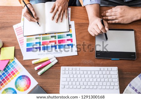 Two colleague creative graphic designer working on color selection and color swatches, drawing on graphics tablet at workplace with work tools and accessories, top view space.