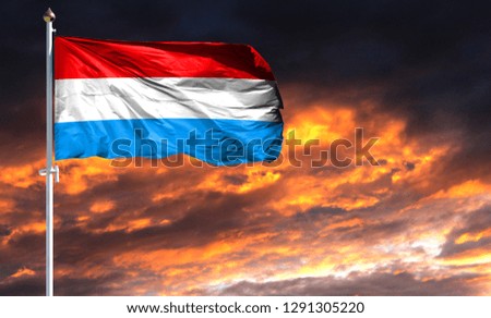 flag of Luxembourg on flagpole fluttering in the wind against a colorful sunset sky
