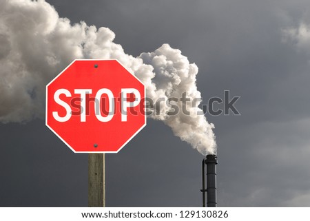 Stop sign in front of smokestack pollution with dark cloud in the background