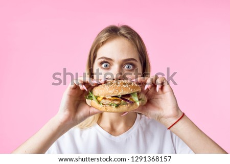 A woman with her eyes wide open holds a hamburger in her hands