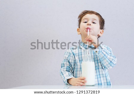 cute happy boy with dark eyes drinks milk from a bottle. the child is wearing a plaid shirt