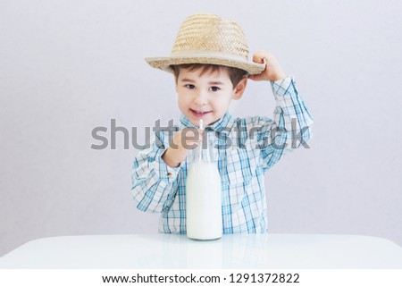 cute happy boy with dark eyes drinks milk from a bottle. checked shirt and hat