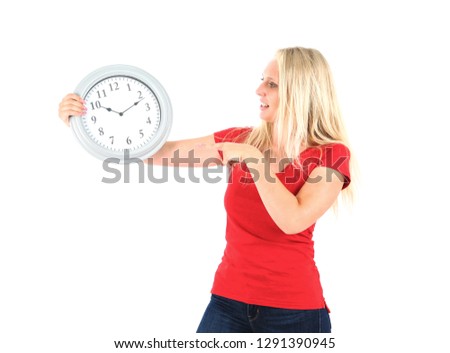 Beautiful blonde woman smiling while holding a clock and pointing at it against a white background