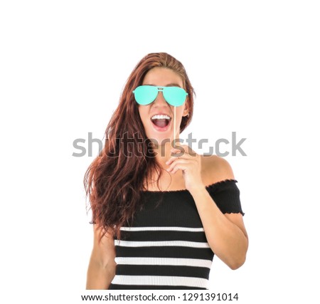 Happy young woman holding a photo booth prop in the shape of blue sunglasses against a white background