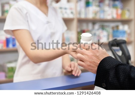 Unrecognizable pharmacist and customer in drugstore. Hand of man taking medicament, client buying in pharmacy. Chemist giving white pill bottle for health care, from disease. Royalty-Free Stock Photo #1291426408
