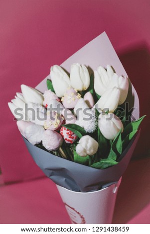 Gift bouquet of white tulips with chocolate covered strawberries at the rose background