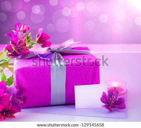Picture of pink luxury gift box with bouquet of beautiful flowers, romantic candle and postcard with text space on the table, festive still life, blurry background, happy mothers day, spring season