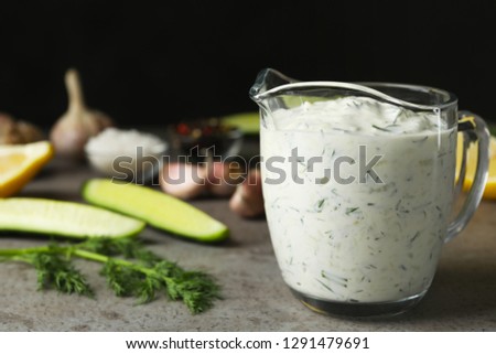 Glass jug of Tzatziki cucumber sauce with ingredients on table. Space for text