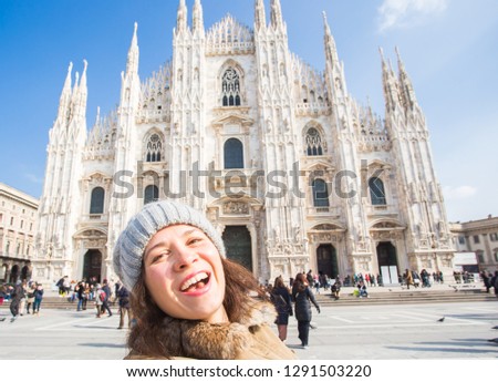 Winter travel, vacations and holidays concept - Young happy woman touris making selfie photo in front of the famous Duomo cathedral in Milan.