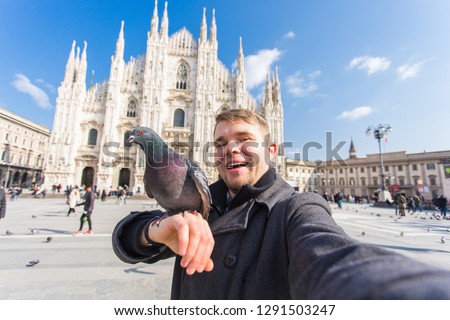 Travel, holidays and winter vacations concept - Happy man take selfie photo with funny pigeons in front of Duomo Milan Cathedral