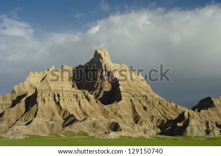 Majestic formation with stark contrast and lush green grass in the foreground. White clouds in the background enhance the feeling of scale.