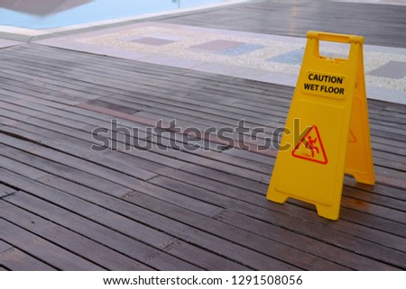 Caution Wet Floor warning yellow sign on wooden floor beside swimming pool