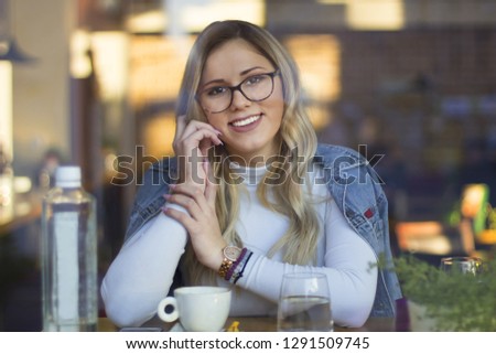 Beautiful blonde girl drink coffee in cafe.View through window.Woman drinking coffee in the morning at restaurant (soft focus on eyes) - Image
