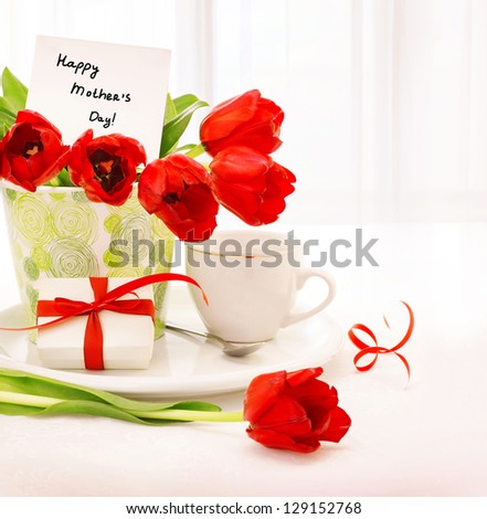 Picture of beautiful tulips pot with gift box and cup of tea on the table at home, breakfast for mommy, happy mothers day, morning drink, romantic still life, indoor decorations, fresh red flowers