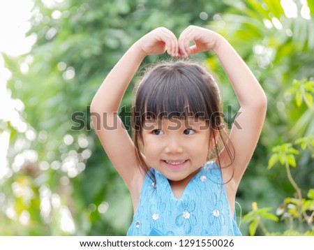 A little Asian girl is posing heart sign arms for her picture.
