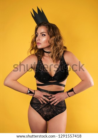 Queen of the drama. Portrait of a beautiful young girl in a black paper crown and in underwear on a yellow background.
