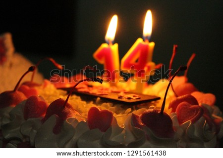 
White cake with a pink heart for a birthday party, along with a candle light, in the dark, blurred background
