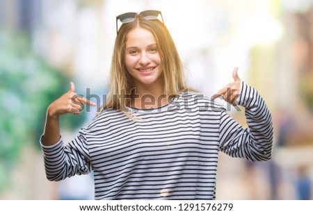 Young beautiful blonde woman wearing sunglasses over isolated background looking confident with smile on face, pointing oneself with fingers proud and happy.