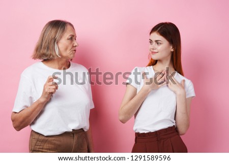 Cute granddaughter and grandmother are standing next to in white T-shirts and chatting on a pink background