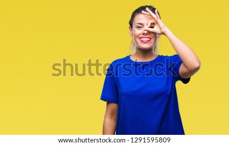 Young beautiful woman wearing casual blue t-shirt over isolated background doing ok gesture with hand smiling, eye looking through fingers with happy face.
