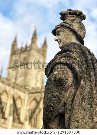 Photo profile of a statue of an historical roman man or soldier with an helmet on the head and a mantel,watching on his left side and showing the elbow of the left arm.A cathedral is in the background Royalty-Free Stock Photo #1291597300