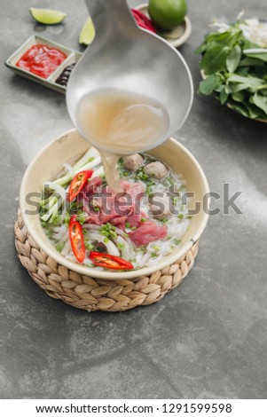 Pho Bo - Vietnamese fresh rice noodle soup with beef, herbs and chili. Stock being poured. Vietnam's national dish.