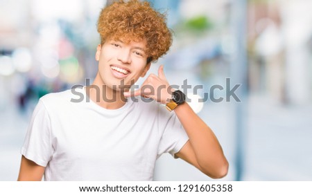 Young handsome man with afro hair wearing casual white t-shirt smiling doing phone gesture with hand and fingers like talking on the telephone. Communicating concepts.