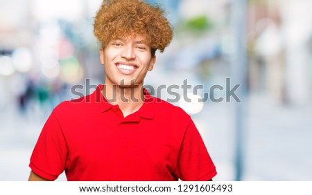 Young handsome man with afro hair wearing red t-shirt Hands together and fingers crossed smiling relaxed and cheerful. Success and optimistic
