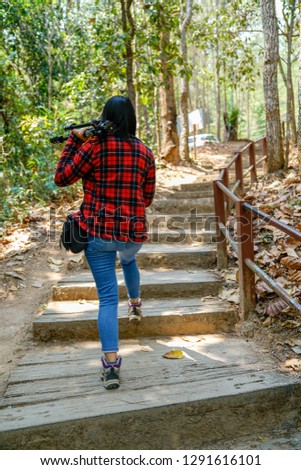 Young photographer lady carrying tripod walk on step to forest