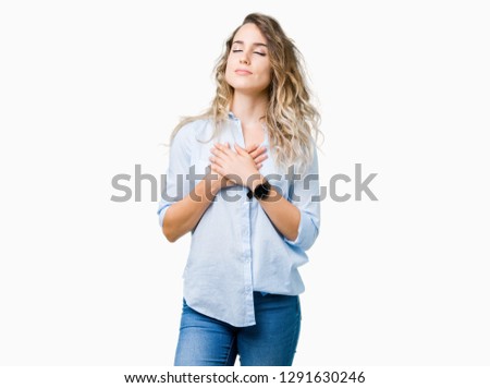 Beautiful young blonde business woman over isolated background smiling with hands on chest with closed eyes and grateful gesture on face. Health concept.