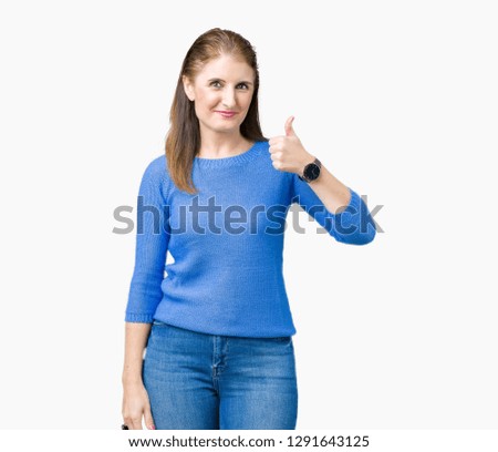 Beautiful middle age mature woman wearing winter sweater over isolated background doing happy thumbs up gesture with hand. Approving expression looking at the camera showing success.