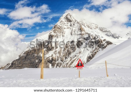 Red triangular sign and fence on white snow on a blurred background of snow-capped mountains