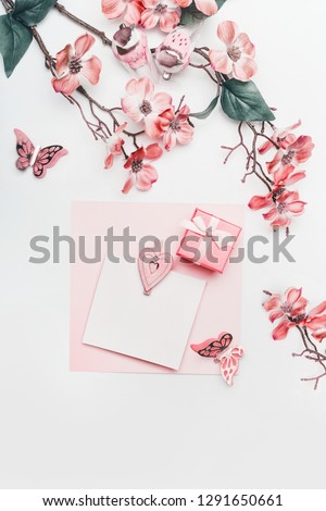 Pretty greeting card mock up in coral color with flowers, ribbon, little gift box and hearts on white background, top view. Flat lay. Abstract love and holidays concept. Blog layout. Pastel color