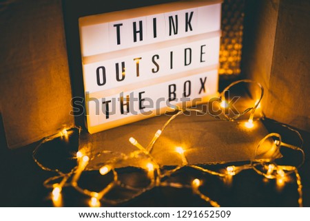Think outside the box message on lightbox next to open parcel with fairy led lights, concept of being unique for success