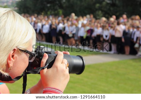 Older woman photographer with digital SLR camera zoom lens taking pictures of school lineup September 1 - photo services, last bell, event photography