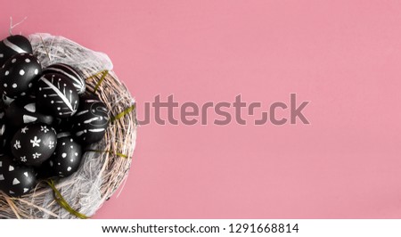 Easter background with eggs in black with a bright pattern handmade in nest of hay on a pink background
