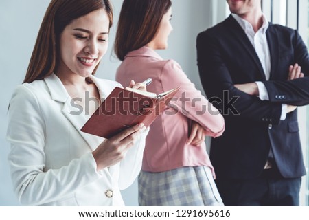Happy young beautiful businesswoman reading book and working in office with colleagues and friend at workplace. Corporate business people group.