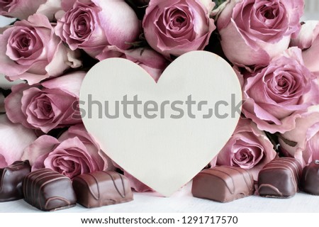 Beautiful retro soft pink rose flower background with wooden heart and room for text surrounded by chocolate candy..