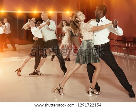 Smiling adult pairs dancing tango movements in modern dance studio 