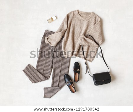 Brown pants in check, beige knitted oversize sweater, cross body bag, black loafers or flat shoes on grey background. Overhead view of women's casual day outfit. Flat lay, top view. Women clothes. Royalty-Free Stock Photo #1291780342