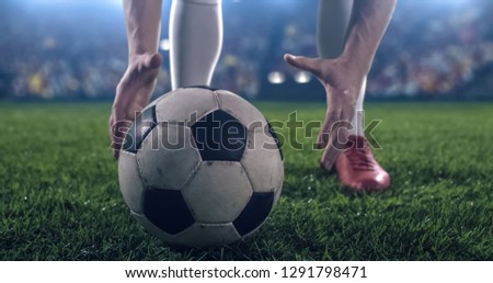 Photo of a soccer player, preparing a ball for a kick. Stadium and crowd are made in 3D.