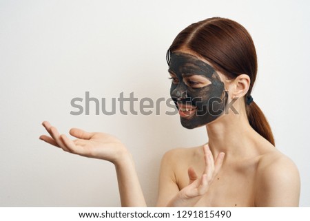 young woman in a cosmetic mask holding a free space on her hand on a light isolated background