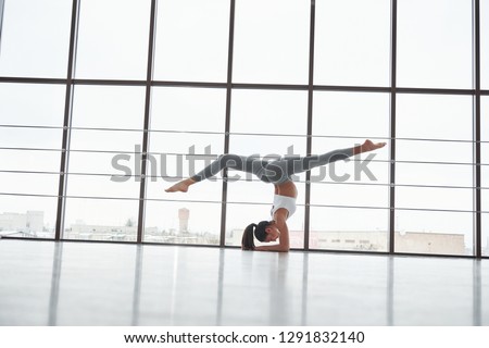 Professional trainer practice her skills. Side view of girl in sportswear doing stretch exercises in the big spacious gym.