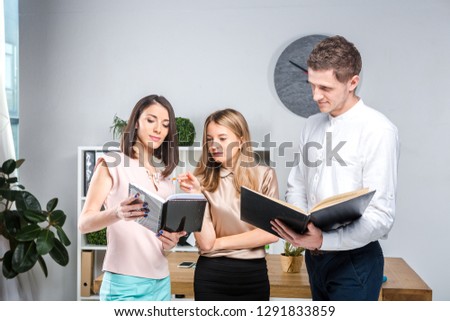 Theme business, teamwork and partnerships. A group of young people, three people, stand in an office near the table in official clothes, work with documents, make praks sign contracts.