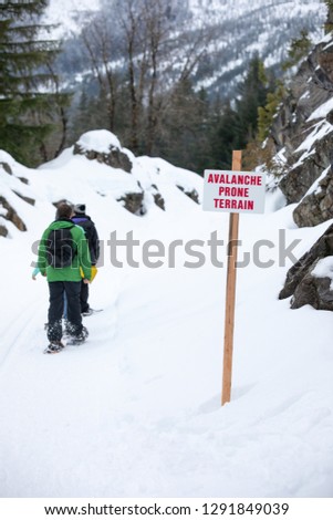 "Avalanche Prone Terrain" sign along a snow covered mountain trail, with snowshoers in the background